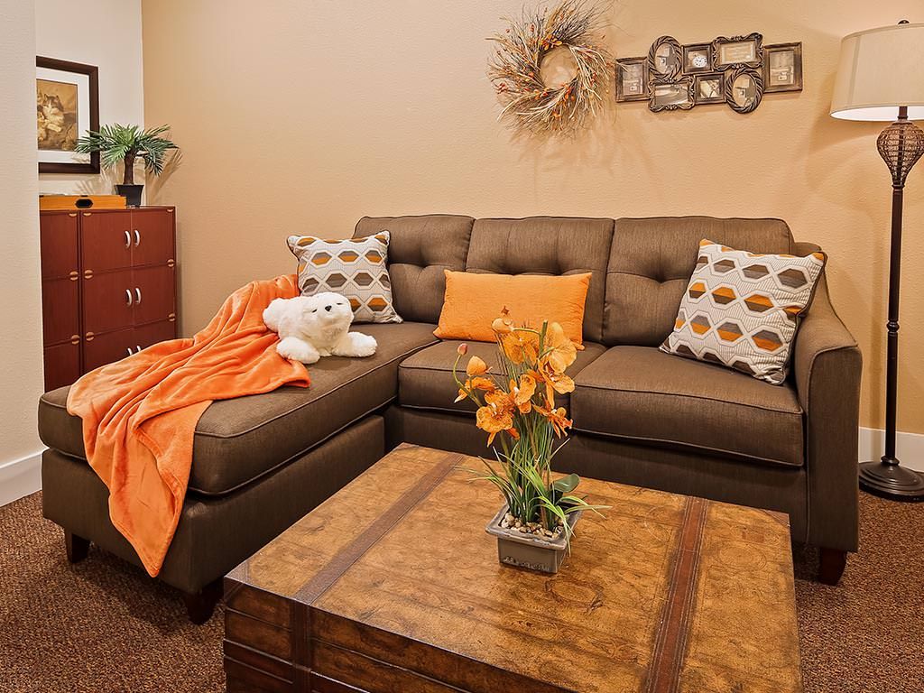 A cozy living room with a brown sofa adorned with decorative pillows and an orange blanket, complemented by a wooden coffee table and wall art.