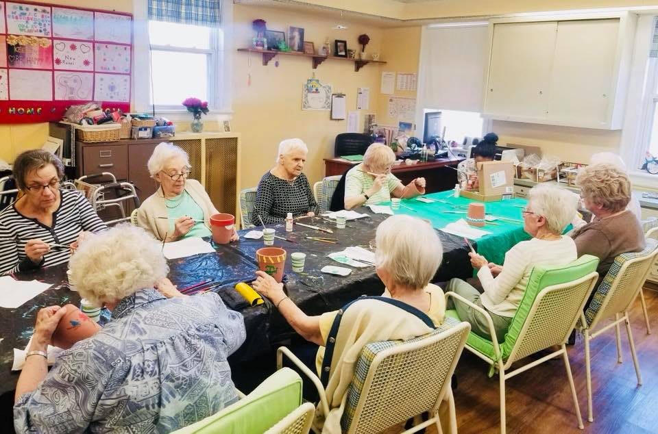 A group of seniors gathered around a table engaged in an activity session indoors.