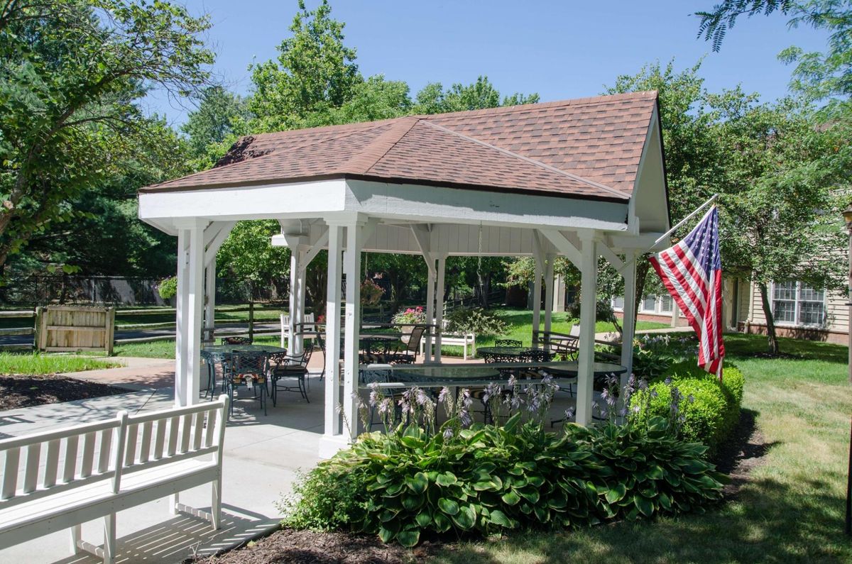 A quaint gazebo in a park setting with benches and an American flag, surrounded by greenery.