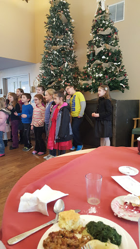 A group of children singing in front of decorated Christmas trees.