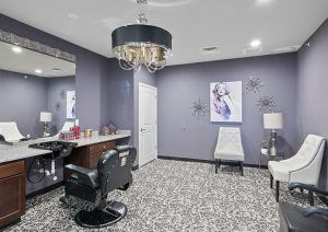 A stylish beauty salon with a modern interior, featuring a chandelier, wall art, and comfortable seating.