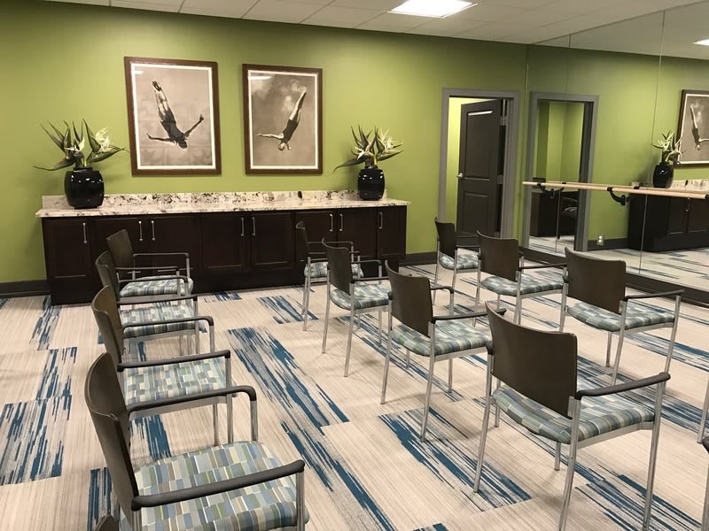An empty waiting room with green walls, decorated with artwork and neatly arranged chairs.