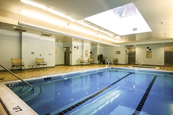 A well-lit indoor swimming pool with a skylight, surrounded by chairs and modern decor.