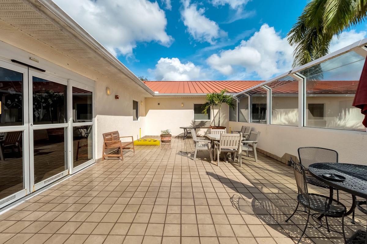 A sunny patio with outdoor seating and tiled flooring, under a blue sky with scattered clouds.
