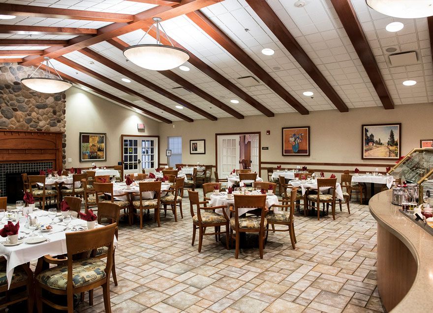 An empty restaurant dining area with neatly arranged tables and chairs, featuring wooden ceiling beams and soft lighting.