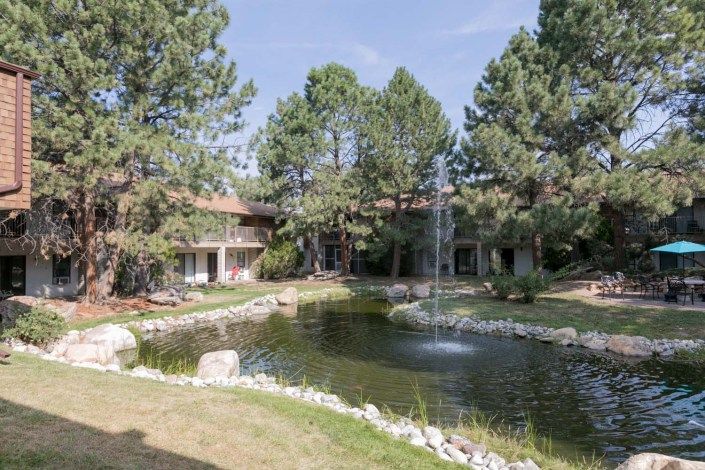 A serene outdoor setting with a pond and fountain surrounded by trees and a building.