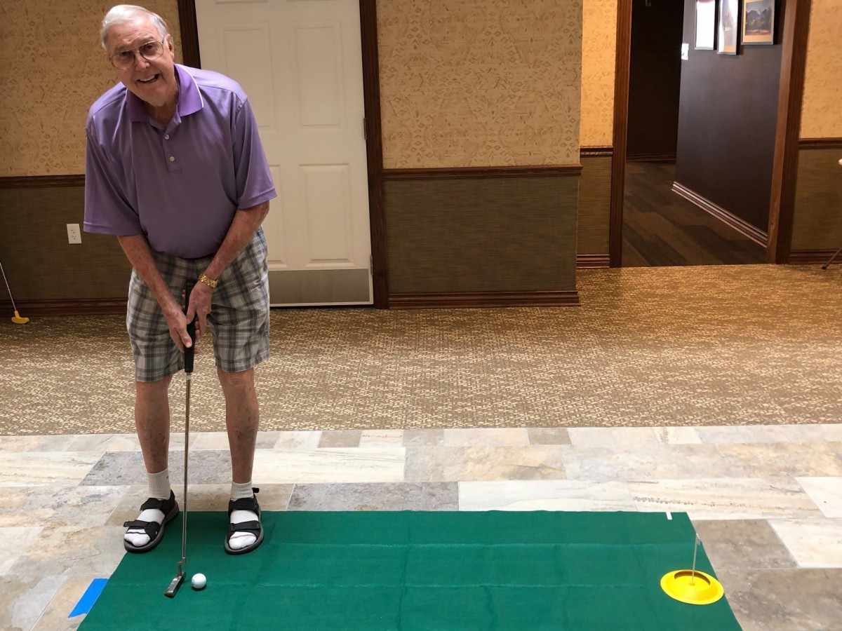 A man practicing indoor golf putting on a carpet.