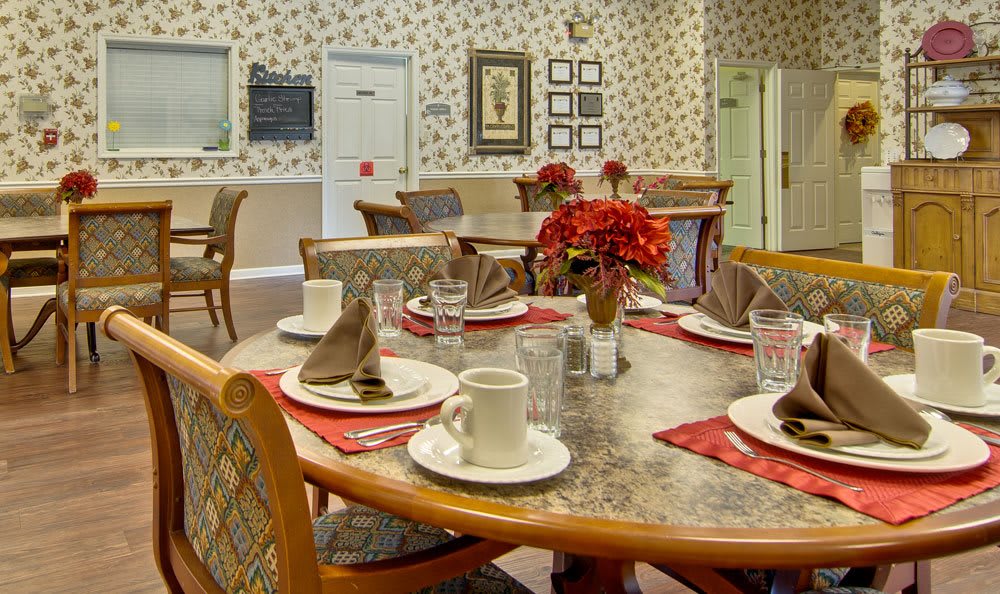 An elegantly set dining table with floral arrangements in a tastefully decorated room featuring floral wallpaper.