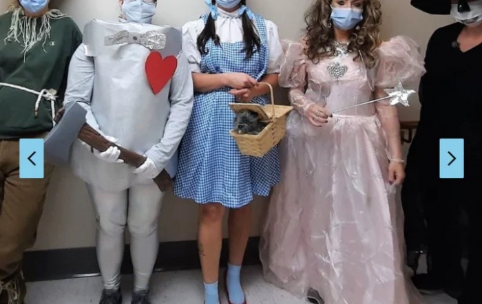 A group dressed in Wizard of Oz costumes, featuring the Tin Man, Dorothy, and Glinda, wearing masks.