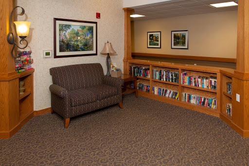 A cozy reading nook featuring a comfortable chair, a lamp, and a bookshelf filled with books.