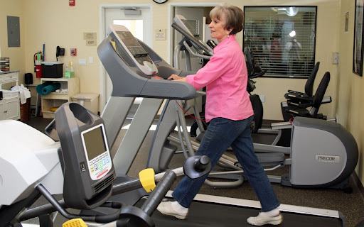 An elderly woman exercises on a treadmill in a gym.