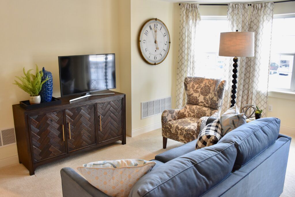 A cozy living room with a sofa, armchair, and television, accented by a large wall clock and floor lamp.
