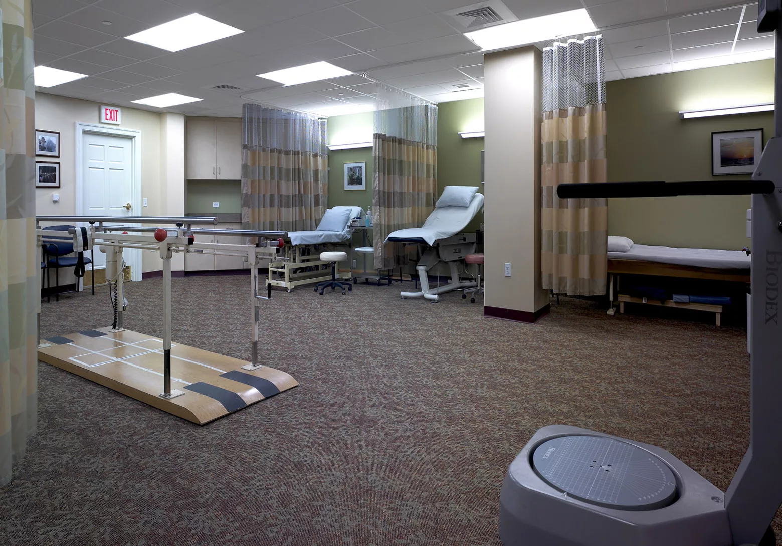 A clinical treatment room with chairs, privacy curtains, and medical equipment.