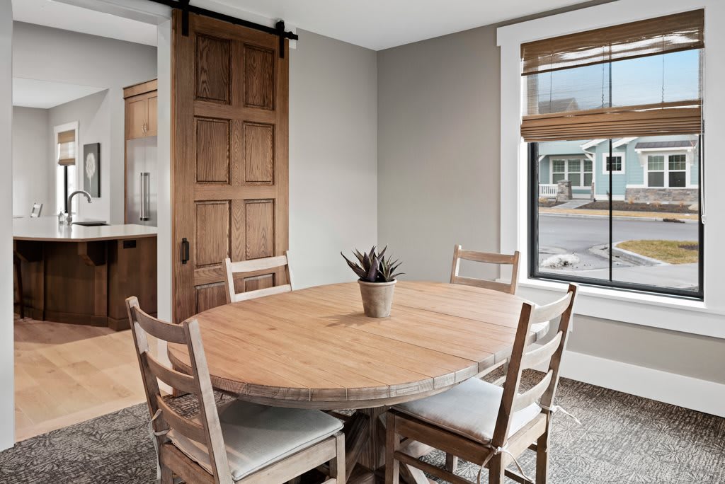 A cozy dining area with a round wooden table, surrounded by matching chairs and illuminated by natural light from a nearby window.