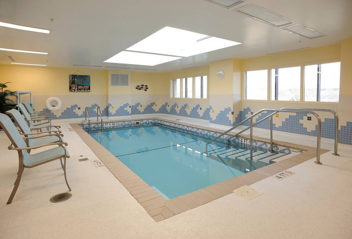 An indoor swimming pool with a beach-themed wall design and ample natural lighting.
