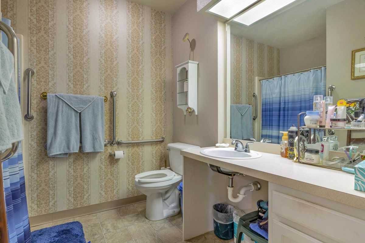 A bathroom interior featuring a sink, toilet, and mirror with patterned wallpaper and a towel rack.