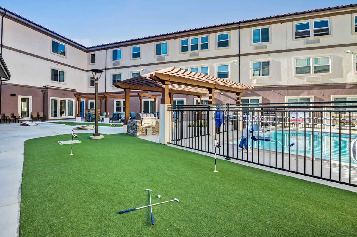 Outdoor area of a hotel featuring a swimming pool, fenced perimeter, and artificial turf with a pergola.