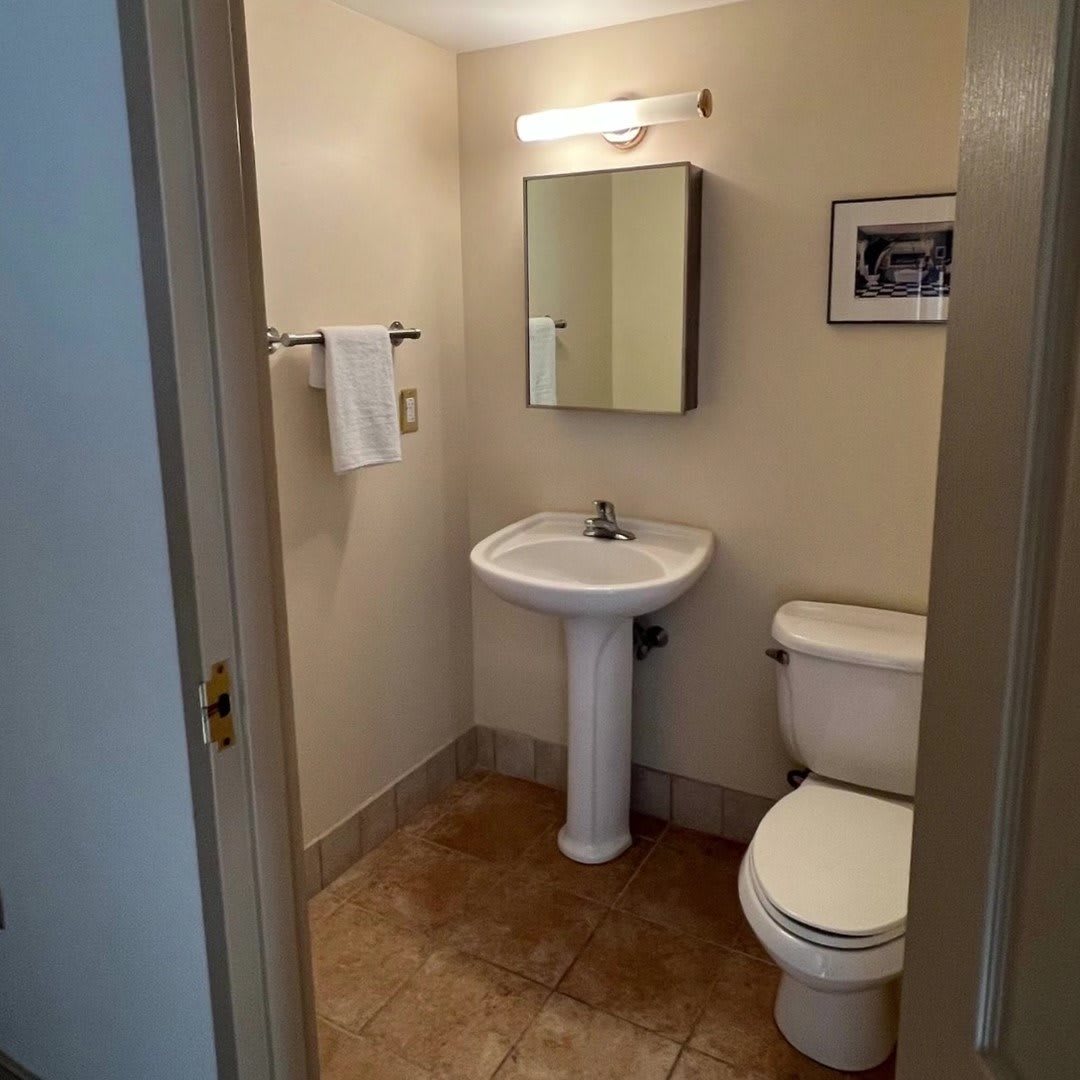A small bathroom featuring a pedestal sink, toilet, and wall-mounted mirror.