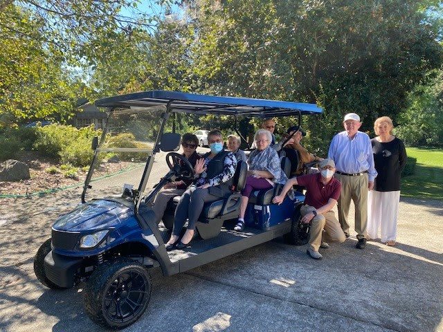 A group of people enjoying a sunny day, gathered around and on a golf cart.