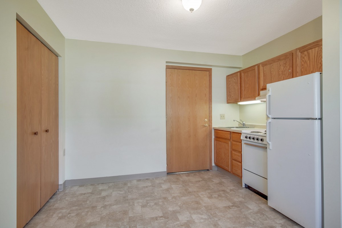A simple kitchen interior in an apartment with a refrigerator, stove, and wooden cabinets.