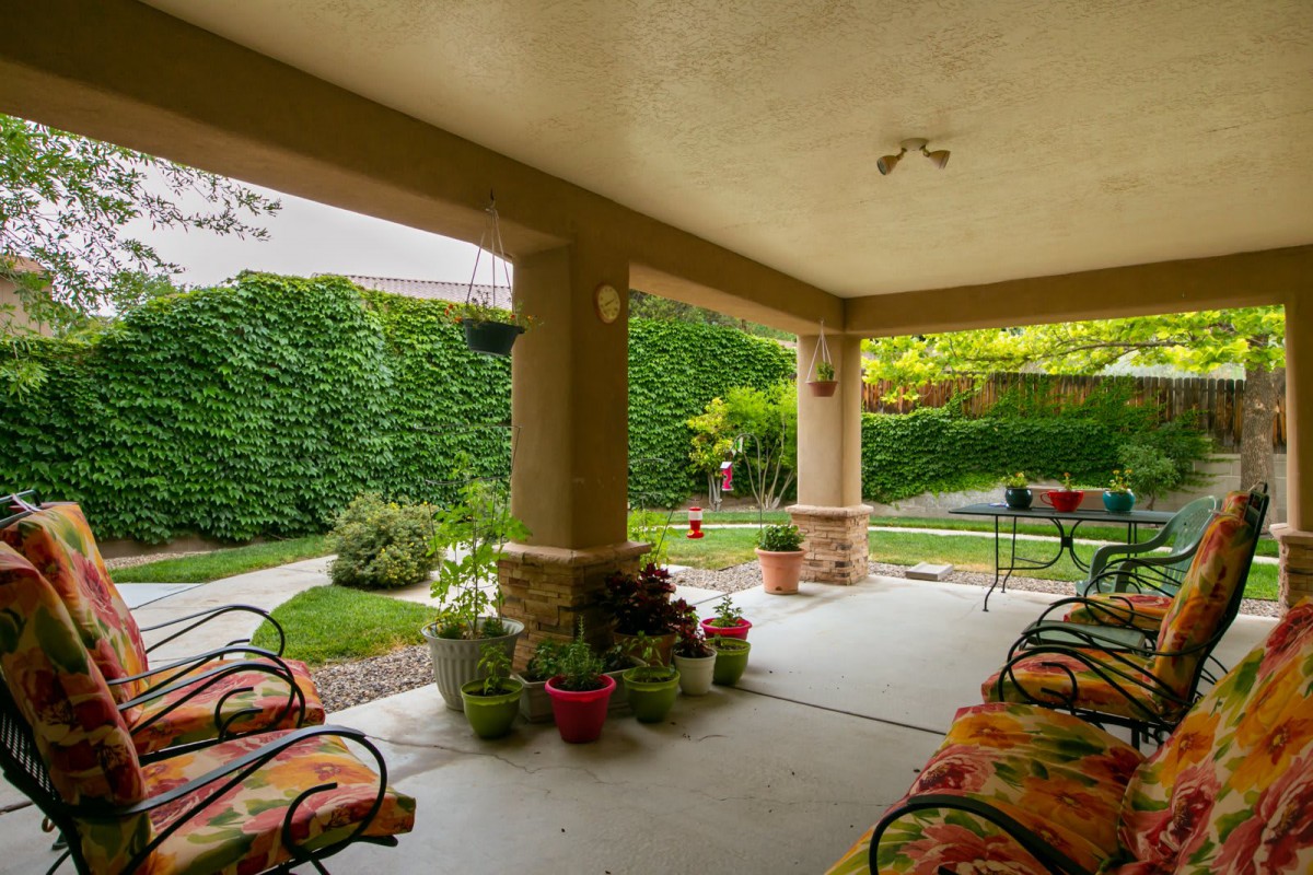 A cozy patio with potted plants and outdoor seating, surrounded by lush garden greenery.