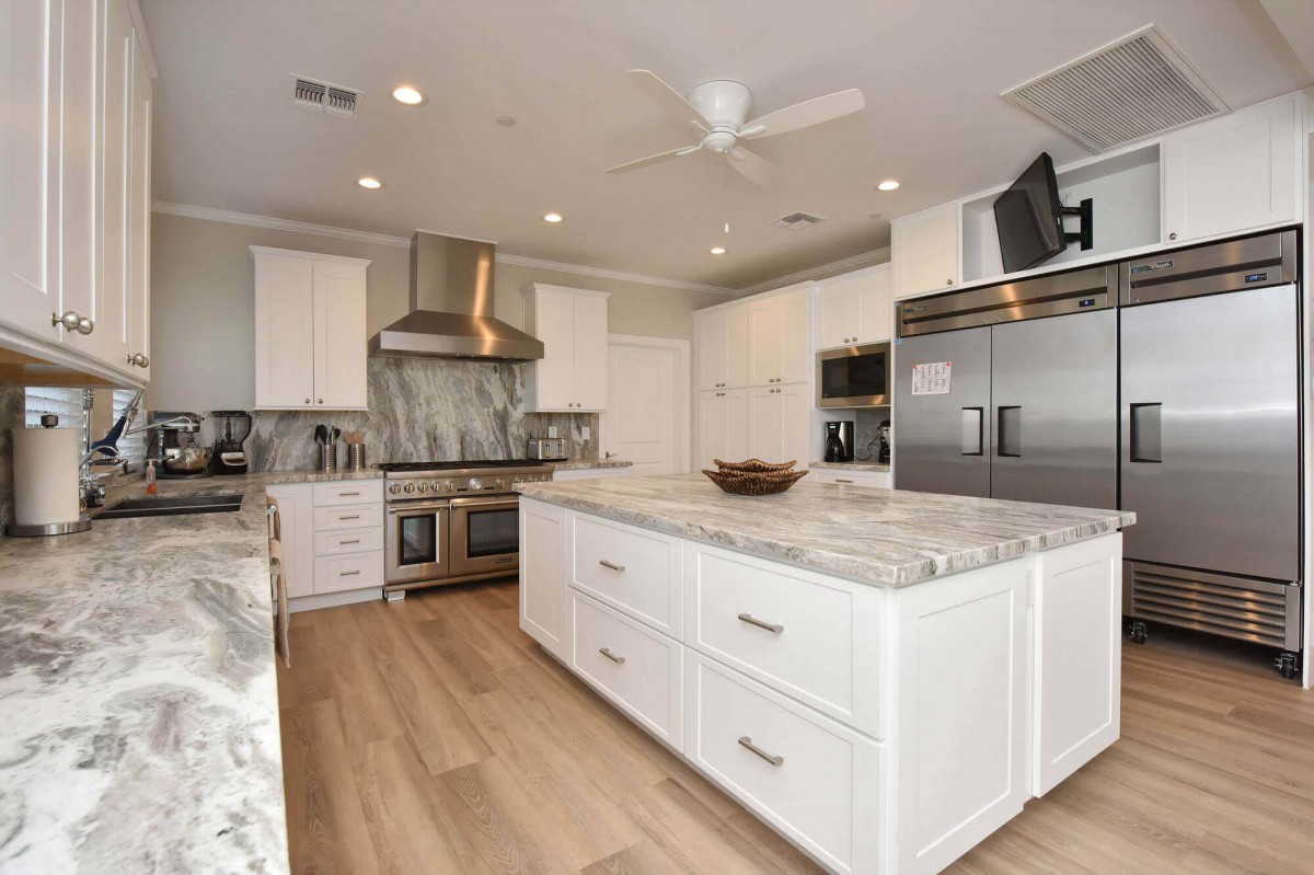A modern kitchen featuring white cabinets, marble countertops, stainless steel appliances, and an island with hardwood flooring.