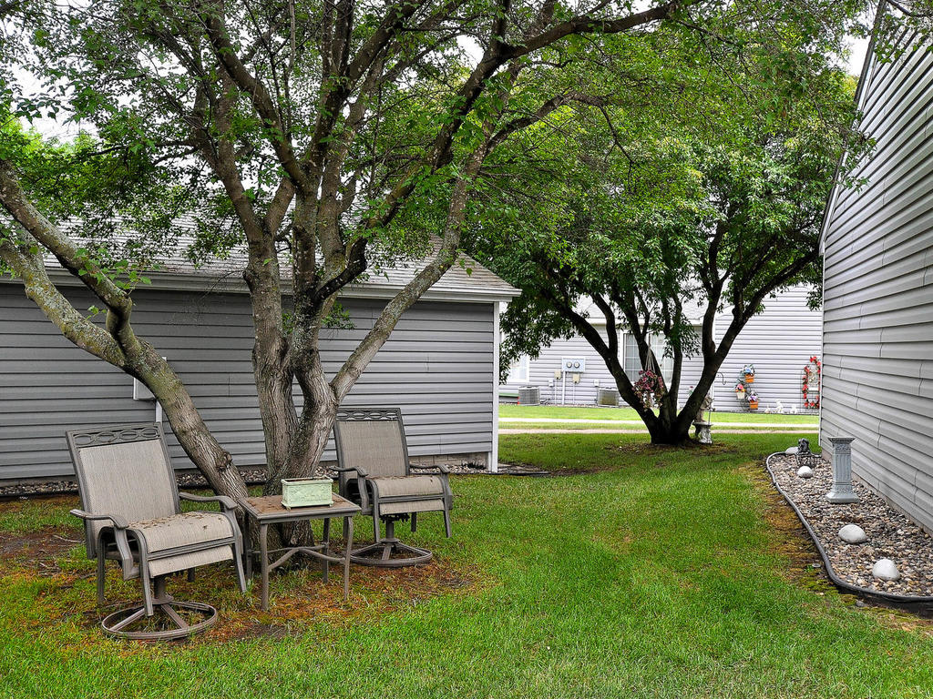 A peaceful backyard scene with chairs under trees beside a shed.