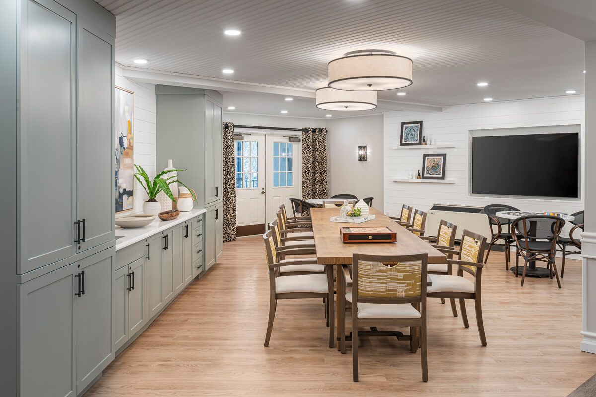 A modern dining room with a long wooden table, surrounded by stylish chairs, featuring elegant lighting and wood flooring.