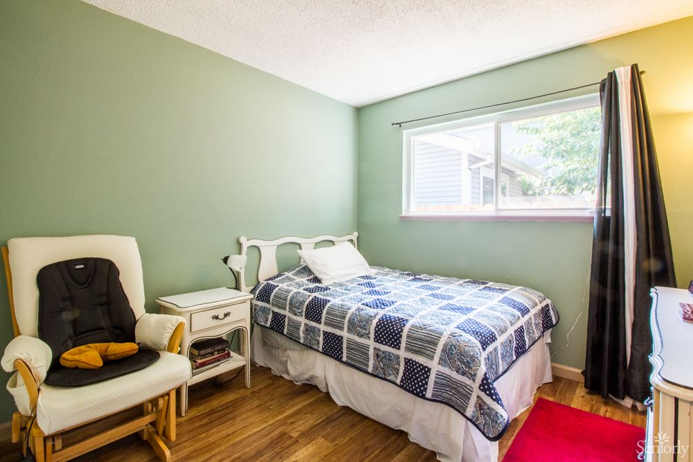 A cozy bedroom with a single bed, green walls, and a wooden floor.