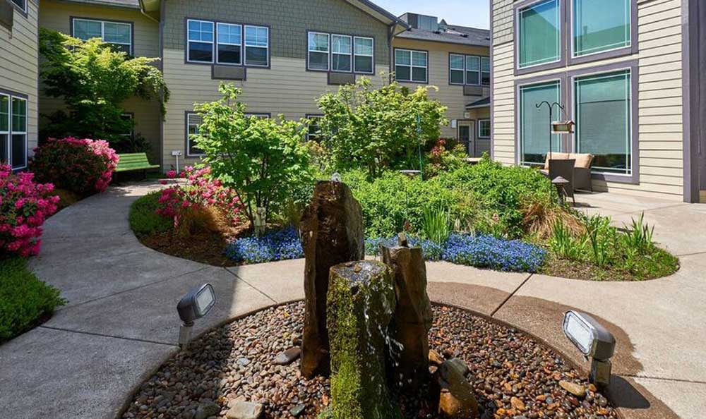 A serene garden with lush greenery and a stone pathway between residential buildings.