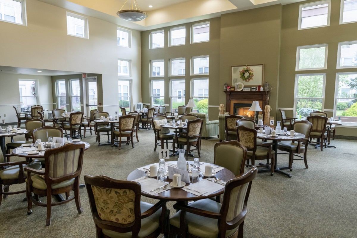 An elegant dining room with neatly set tables, comfortable chairs, large windows, and a cozy fireplace.
