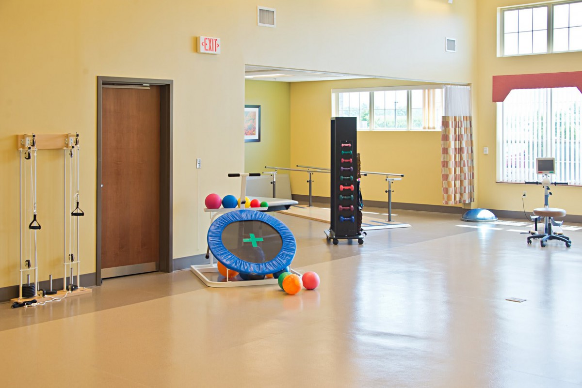 A therapy room equipped with various exercise equipment including a small trampoline and colorful balls.