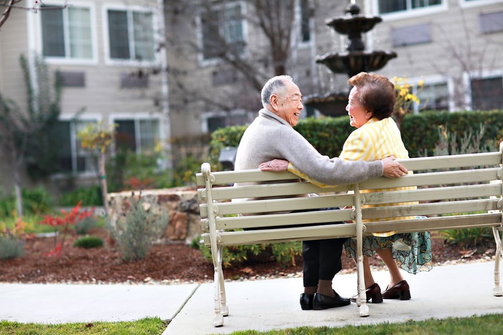 An elderly couple sits together on a park bench, enjoying the serene garden view.