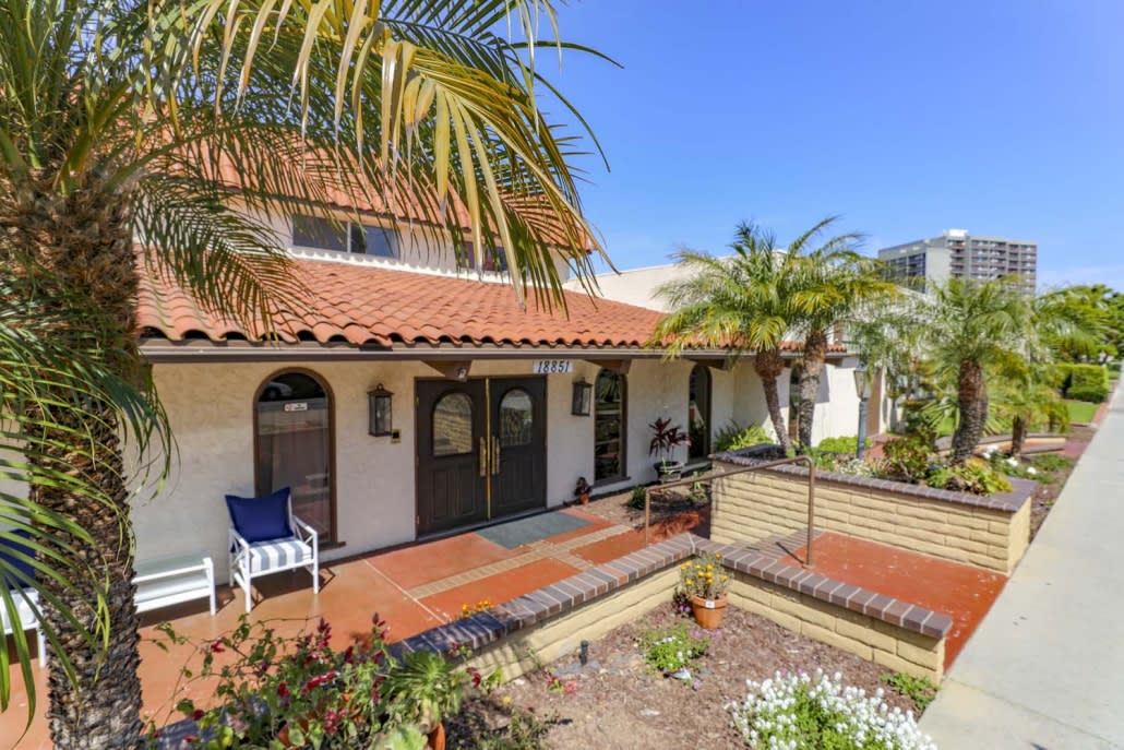A Spanish-style house with a terracotta roof and a patio surrounded by palm trees.