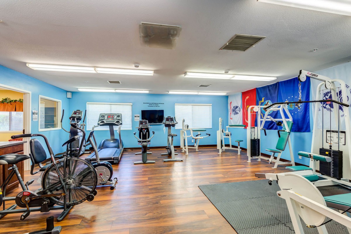 A well-equipped gym with various exercise machines and weights on a wooden floor.