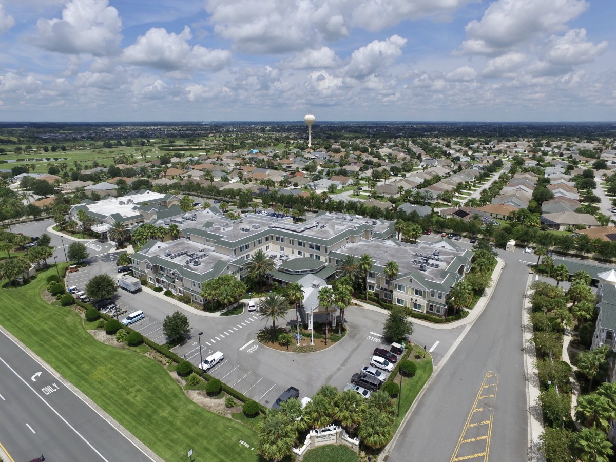 Aerial view of a suburban area with buildings, a parking lot, and surrounding roads under a cloudy sky.
