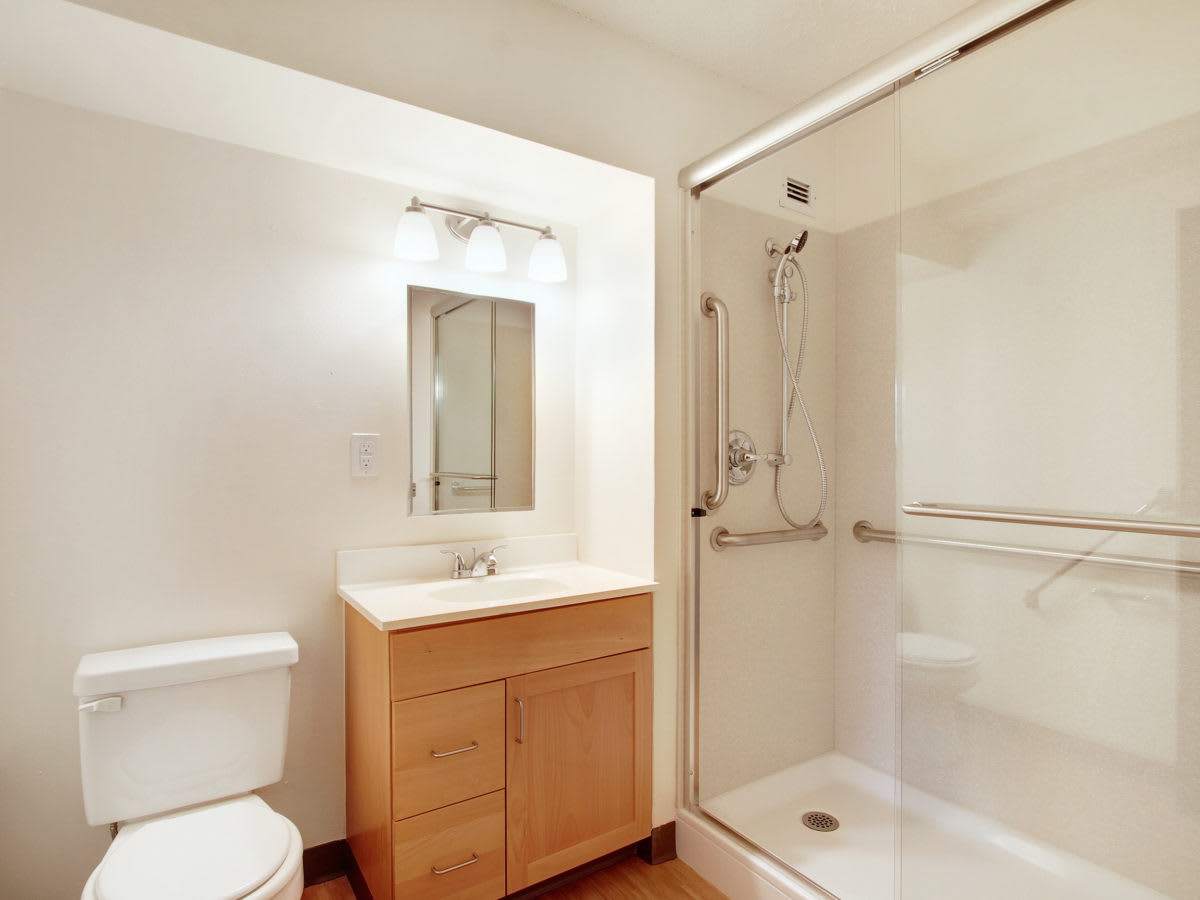 A modern and minimalist bathroom featuring a shower with glass doors, a sink with a wooden cabinet, and a toilet.