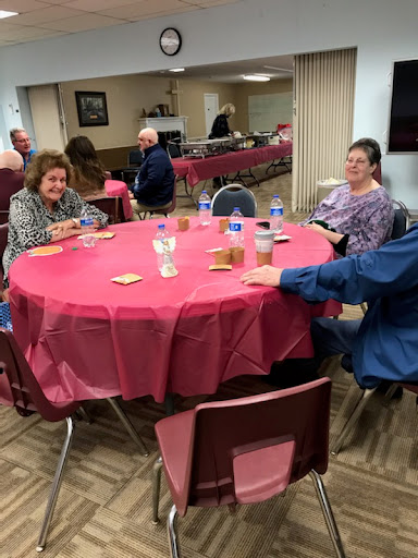 A social gathering of seniors around tables with red tablecloths, engaging in conversation.