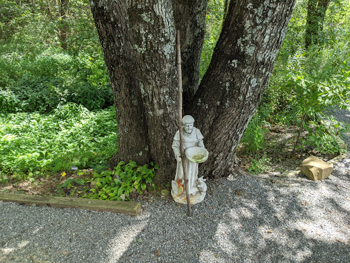 A serene stone statue stands beside a large tree, surrounded by lush greenery.