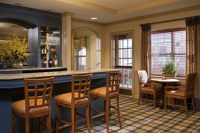 A cozy bar interior featuring a counter with wooden chairs and a side table by the windows.