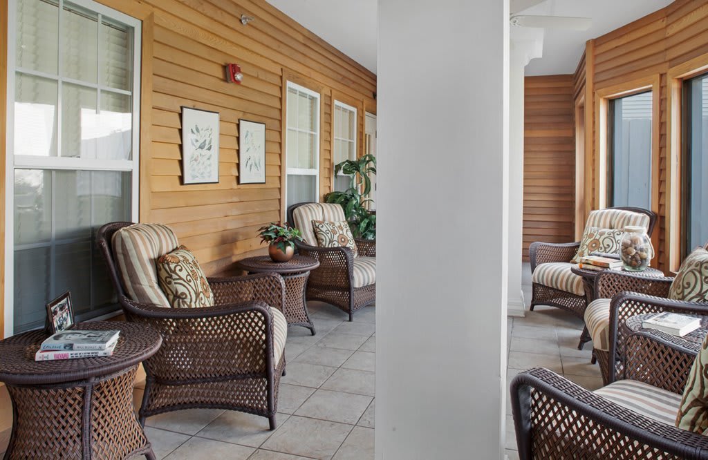 A cozy porch area with wicker chairs and cushions, featuring wood paneling and decorative elements.