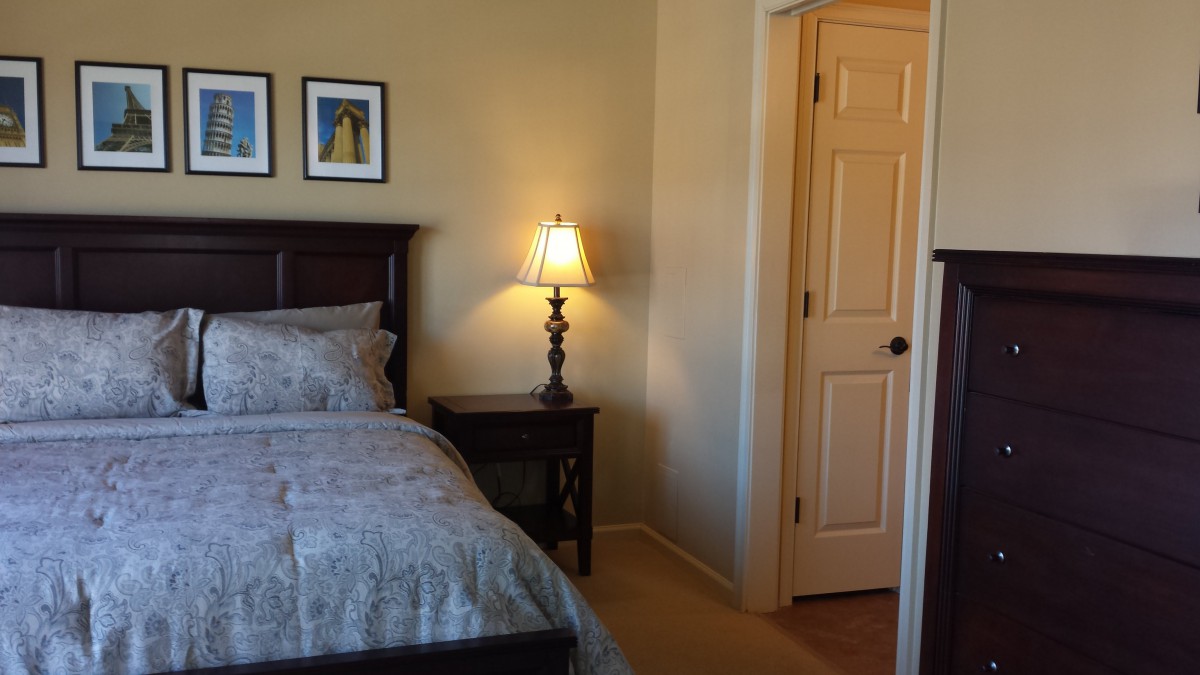 A cozy bedroom with a bed, nightstand, and lamp next to a door.