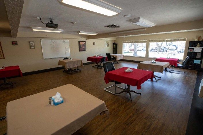 An empty classroom with tables and chairs, featuring a whiteboard and projector.