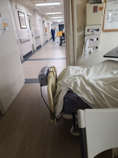 A view inside a hospital patient room, showcasing the bed with a patient and healthcare staff in the hallway.