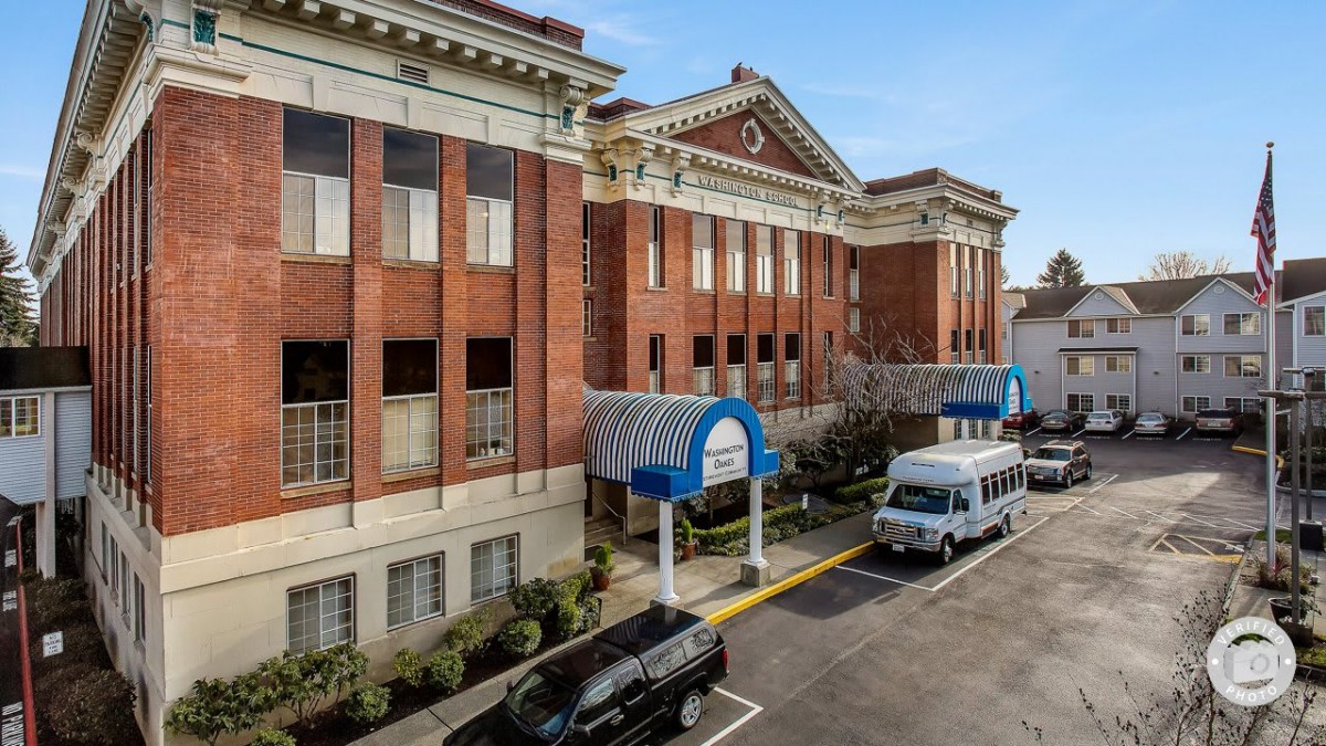 A hospital building with a covered entrance and parked vehicles.