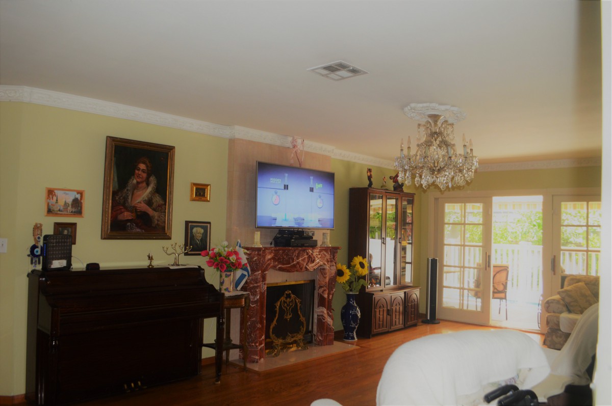 A cozy living room featuring a chandelier, fireplace, and piano, with decorative elements including sunflowers and a wall-mounted television.