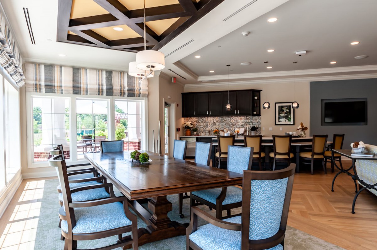 A stylish dining room with a large wooden table and blue upholstered chairs, connected to an open kitchen area.