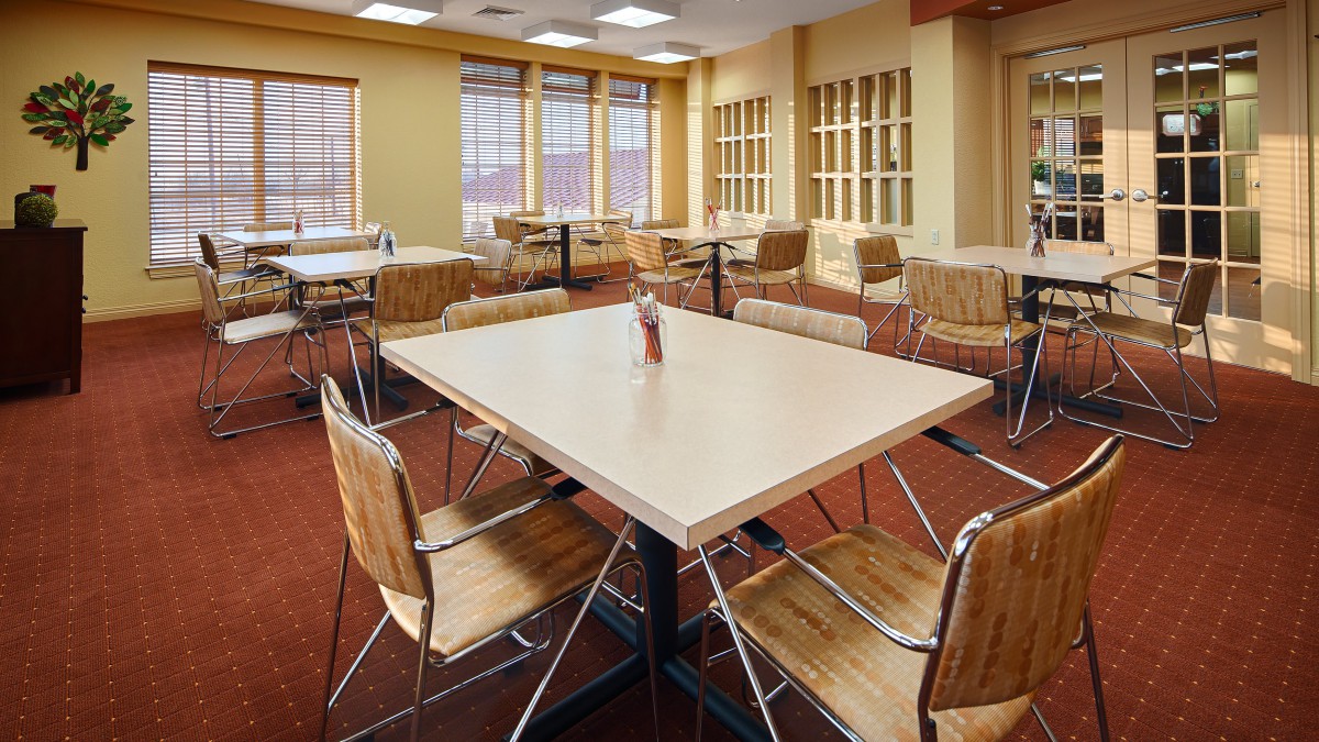 An empty cafeteria with wooden tables and chairs, well-lit by overhead lights.