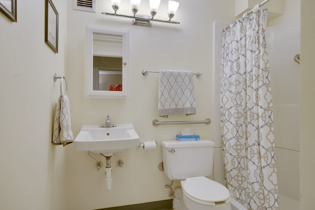 A well-lit bathroom with a sink, mirror, toilet, and shower area.