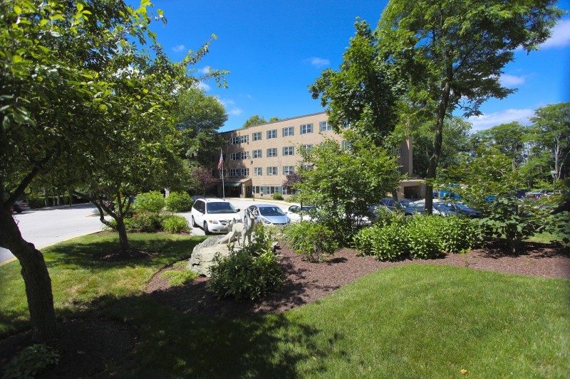 A sunny day with a building surrounded by trees, cars, and well-maintained landscaping.
